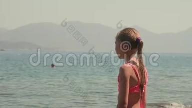年轻的女孩穿着粉红色的泳衣，在阳光明媚的海滩上看着<strong>大海</strong>的<strong>风景</strong>。 海山少女肖像画